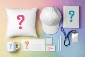 flat lay of blank white branded merch and business materials including a cushion, envelope and hat on a rainbow colored surface