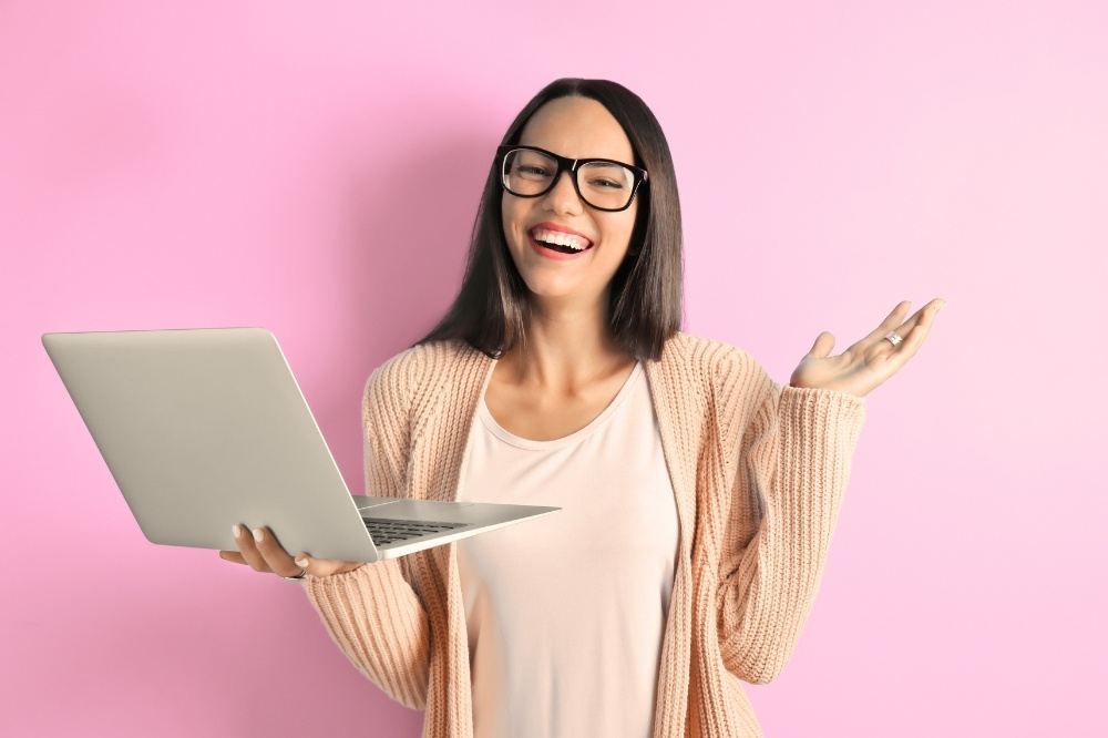 happy woman with holding open laptop against pink background