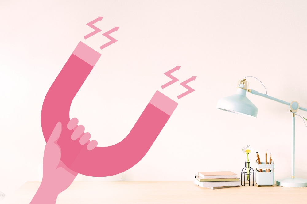 pink graphic of hand holding a magnet with a photo background of a stylish work desk