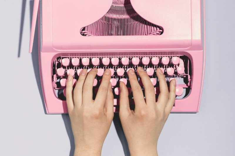 hands typing on a pink retro typewriter